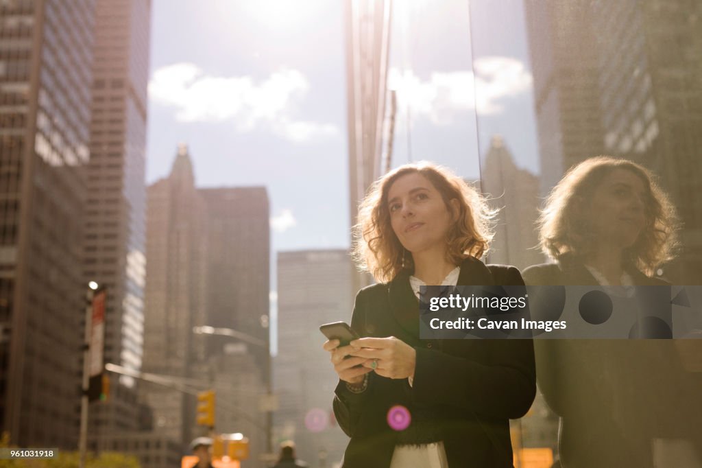 Woman using mobile phone while leaning on building in city
