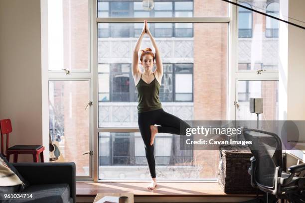 portrait of confident woman practicing tree pose by window at home - tree position stock pictures, royalty-free photos & images