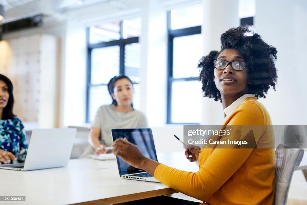 Businesswoman looking over shoulder while working on laptop computer with female colleagues in background