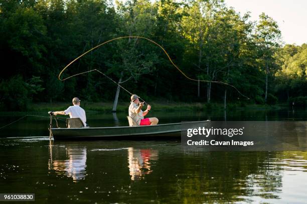 man casting fishing line in lake with friend sitting in rowboat - boat side view stock pictures, royalty-free photos & images