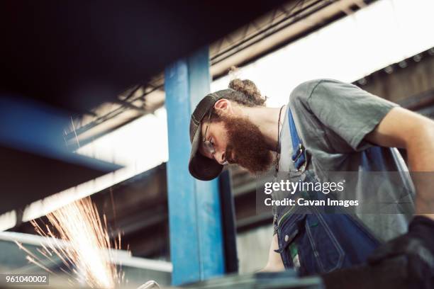 low angle view of blue collar worker using welding machine in steel industry - foundry stock-fotos und bilder