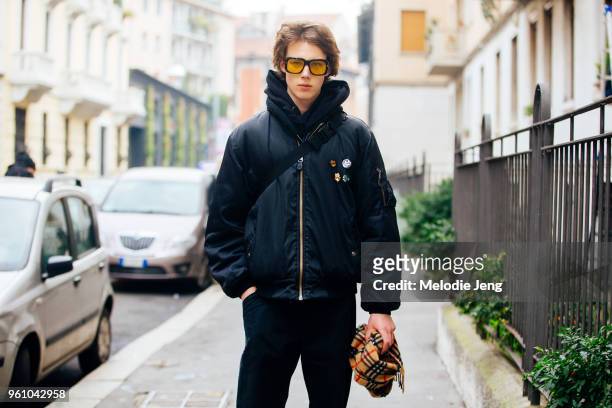 Model Vincent Holden wears yellow-tinted sunglasses, a black bomber jacket with pins, and holds a yellow Burberry check scarf during Milan Men's...