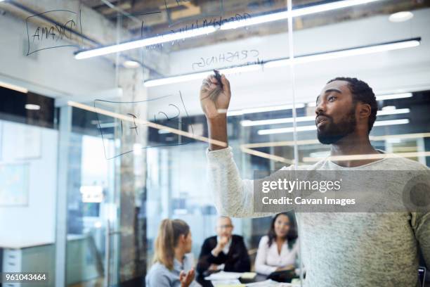 confident businessman writing on felt tip pen while colleagues sitting in background during meeting at office - felt tip pen stock-fotos und bilder