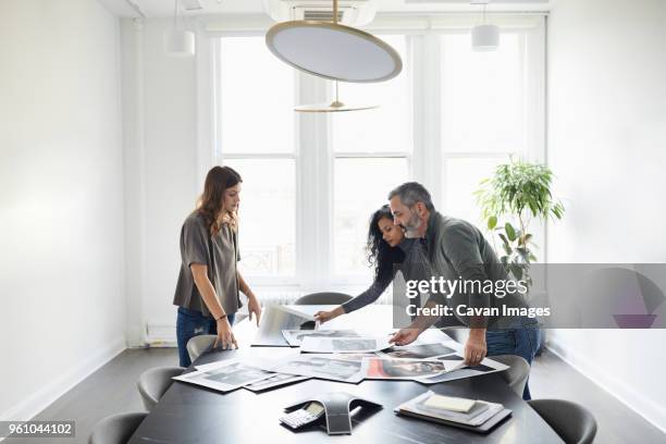 business people examining photograph printouts in conference room - printout stock pictures, royalty-free photos & images