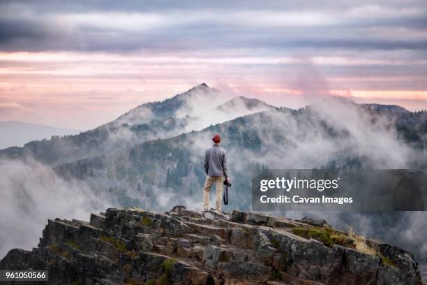 rear view of photographer standing on cliff against cloudy sky - klippe stock-fotos und bilder