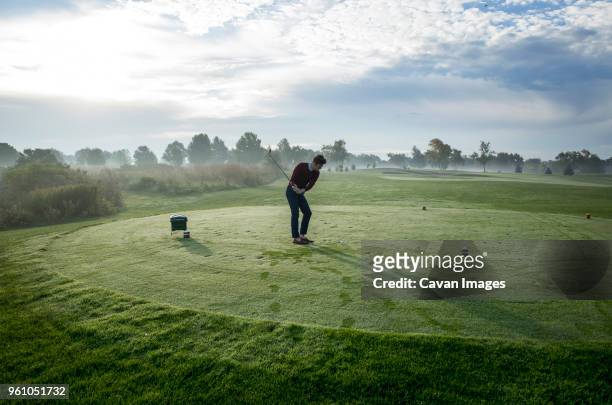 man playing golf on field against sky on sunny day - golf swing foto e immagini stock