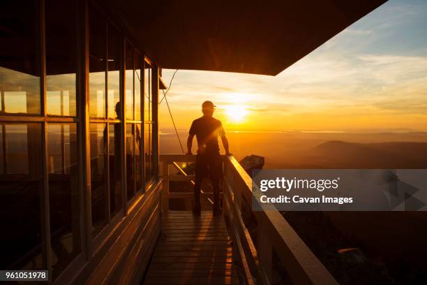 rear view of hiker standing at fire lookout tower during sunset - uitkijktoren stockfoto's en -beelden