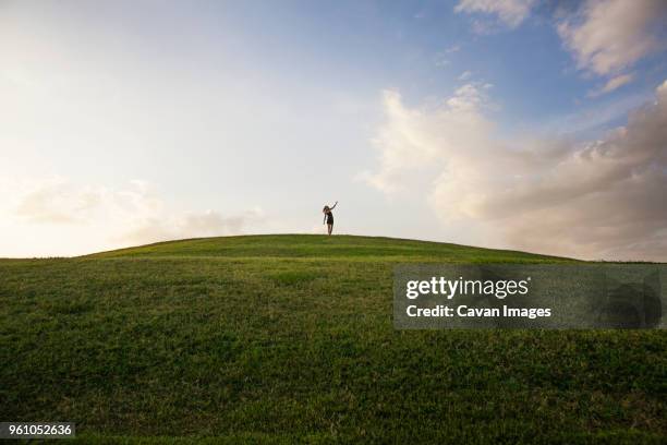 distant view of woman standing on grassy field against sky - person standing far stock pictures, royalty-free photos & images