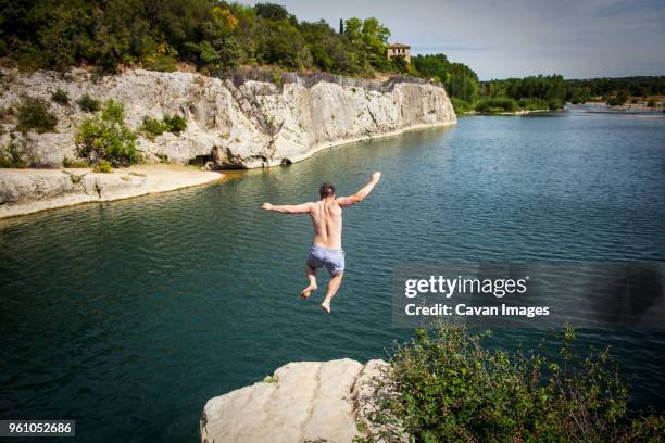 rear view of man diving off rock into river - salto desde acantilado fotografías e imágenes de stock