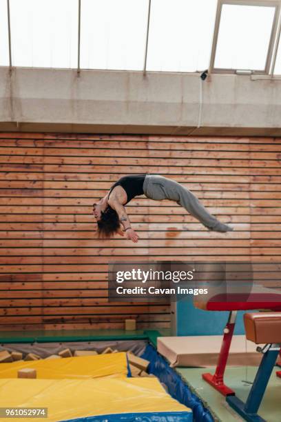 side view of gymnast jumping from gymnastics equipment at gym - gymnastics equipment stock pictures, royalty-free photos & images