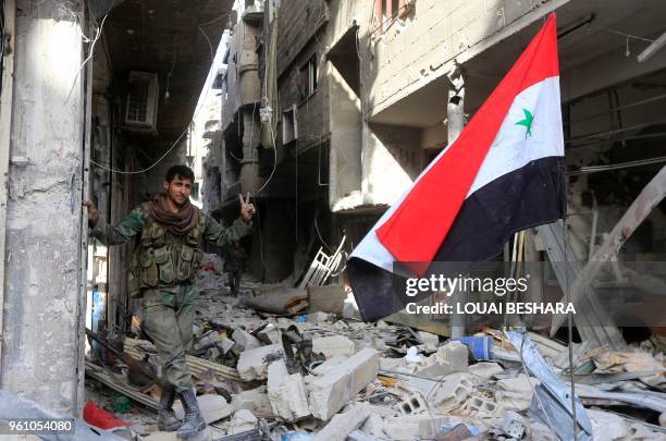 Member of the Syrian government forces poses for a photo next to a Syrian flag in destroyed buildings at the entrance of the Palestinian camp of...