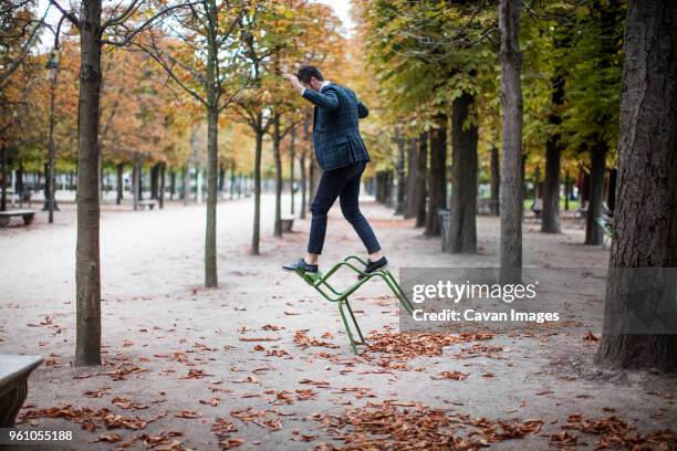 full length of businessman playing on chair at park - standing on chair stockfoto's en -beelden