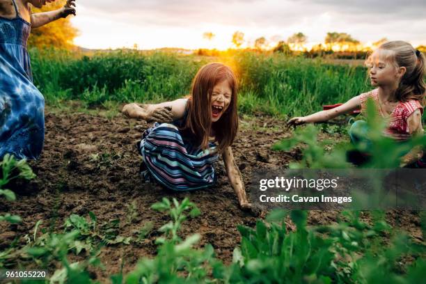 girl with sisters shouting while crouching in mud - kids mud stock pictures, royalty-free photos & images