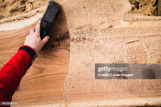 cropped hand of carpenter cleaning sawdust on wooden plank at backyard - sägemehl stock-fotos und bilder