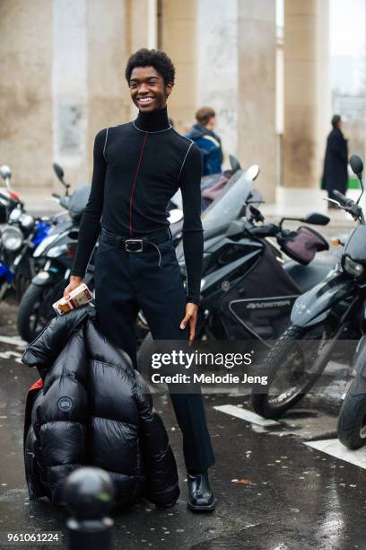 Model Alton Mason wears an all black outfit including a fitted turtleneck, Canada Goose puffer jacket and a Moschino cigarette phone case during...