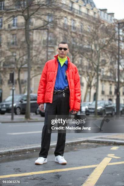 Model Simon Bornhall wears futuristic small Matrix-style black sunglasses, a red puffer jacket, blue shirt, neon turtleneck, black windowpane...