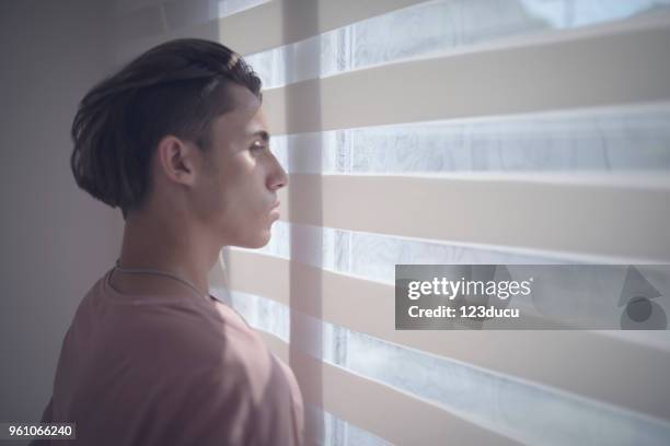 young sad man looking out window - 123ducu stock pictures, royalty-free photos & images