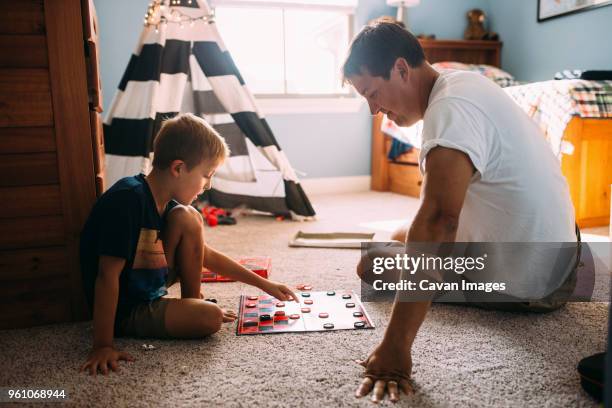 father and son playing checkers while sitting on carpet at home - checkers game ストックフォトと画像