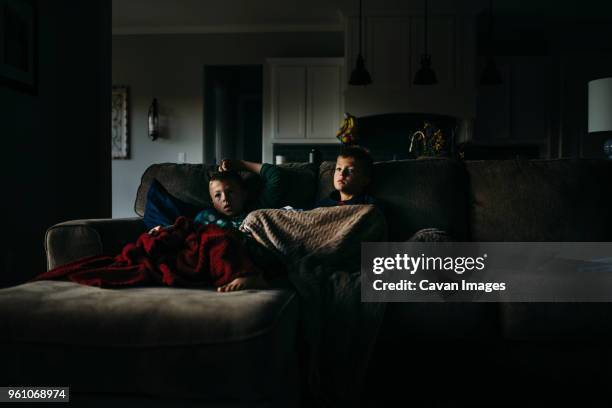 brothers under blankets watching tv while sitting on sofa at home in darkroom - dark room stock-fotos und bilder