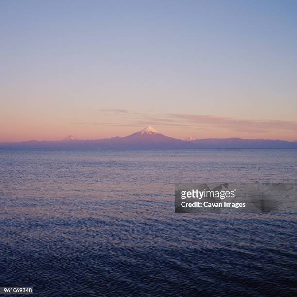 scenic view of lake by snowcapped mountain against sky - llanquihue lake stock-fotos und bilder