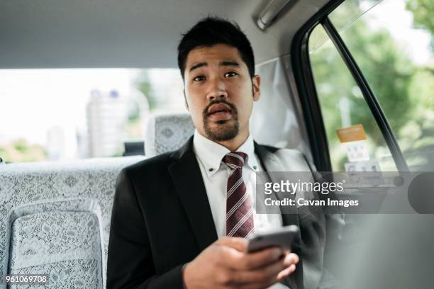 young businessman holding smart phone while sitting in taxi - businessman taxi stock-fotos und bilder