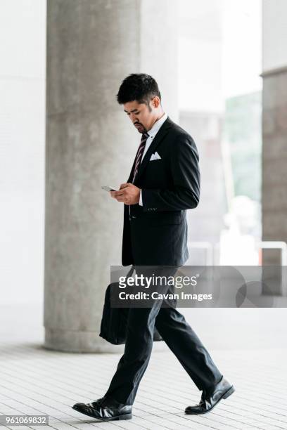 full length of businessman using smart phone while walking at colonnade - business man walking with a bag in asia bildbanksfoton och bilder