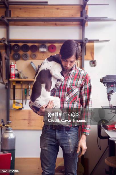 young man carrying dog while standing at workshop - tool rack stock pictures, royalty-free photos & images