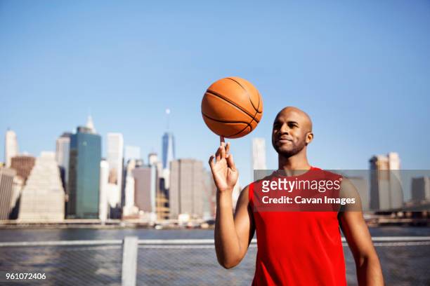 smiling man spinning basketball on finger against city skyline - usa 2016 basketball man 個照片及圖片檔