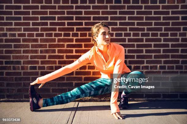 determined female athlete stretching on footpath against brick wall - dedication brick stock pictures, royalty-free photos & images