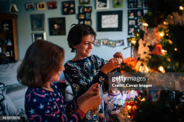 siblings decorating christmas tree at home - kerstboom versieren stockfoto's en -beelden