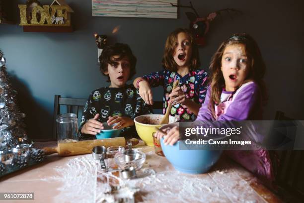 surprised siblings looking away while making dessert at home - alleen kinderen stockfoto's en -beelden