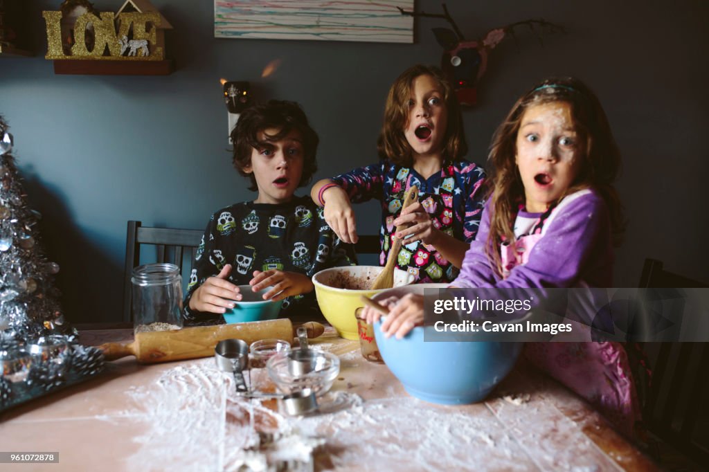 Surprised siblings looking away while making dessert at home