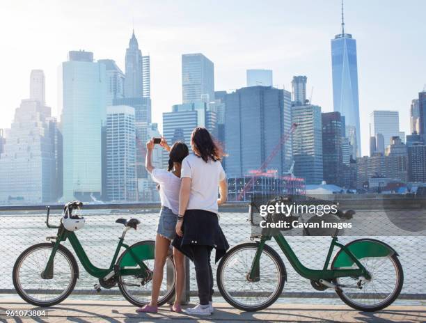 rear view of couple photographing cityscape by river - new york tourist stock-fotos und bilder