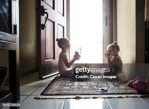 Sister in ballet costumes holding cameras while sitting at doorway Sister in ballet costumes holding cameras while sitting at doorway