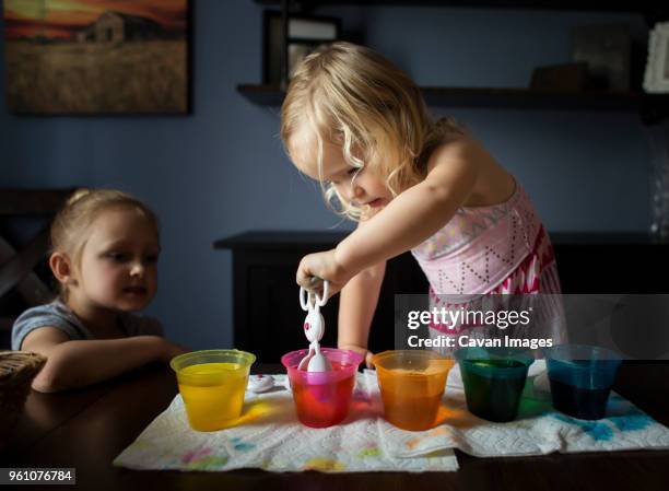 girl looking at sister preparing easter eggs on table at home - sister imagens e fotografias de stock