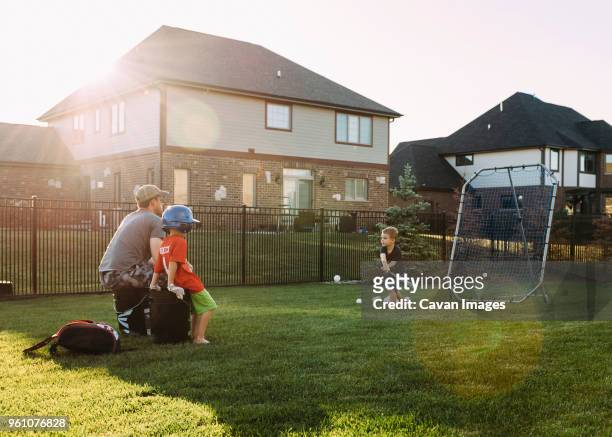 family playing baseball at backyard on sunny day - backyard baseball stock-fotos und bilder