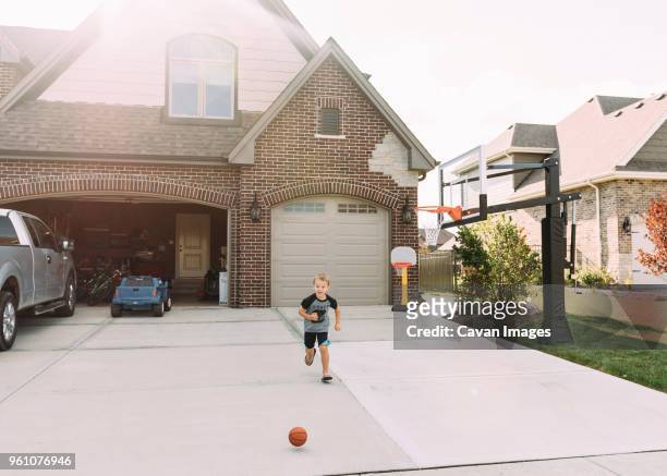 boy running behind basketball on driveway - garage driveway stock pictures, royalty-free photos & images