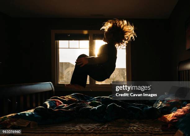 playful boy jumping on bed at home - a boy jumping on a bed fotografías e imágenes de stock