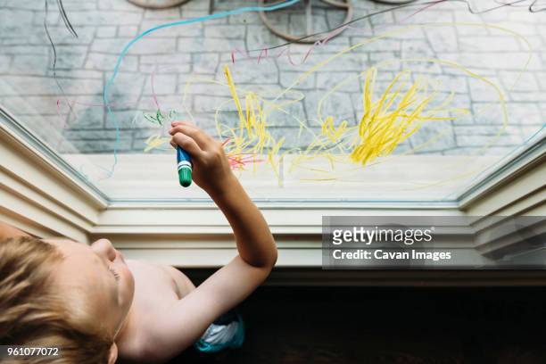 overhead view of shirtless boy writing on window at home - kid with markers 個照片及圖片檔