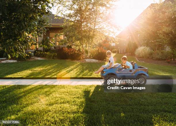 siblings playing with toy car on sidewalk at yard - speelgoedauto stockfoto's en -beelden