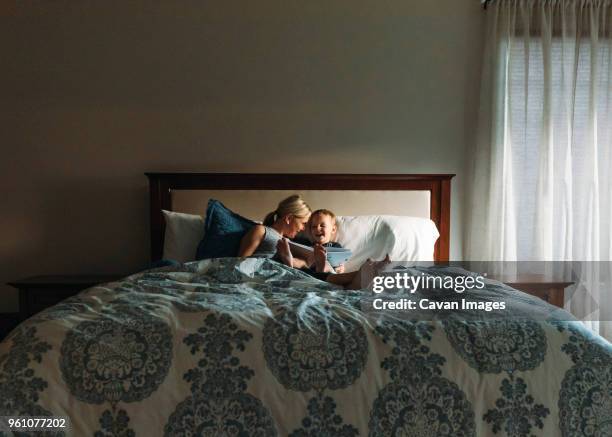 happy mother and son reading book while relaxing on bed - story stock pictures, royalty-free photos & images