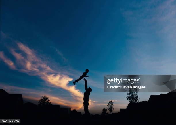 silhouette father throwing son into air against sky during dusk - dad throwing kid in air imagens e fotografias de stock