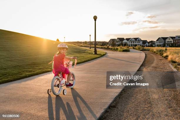 portrait of girl riding bicycle on road against sky - training wheels stock pictures, royalty-free photos & images