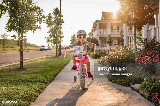 playful girl wearing sunglasses while riding bicycle - stützrad stock-fotos und bilder