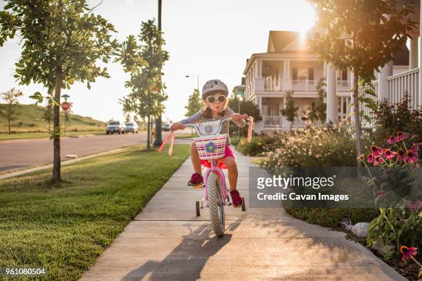playful girl wearing sunglasses while riding bicycle - training wheels stock pictures, royalty-free photos & images
