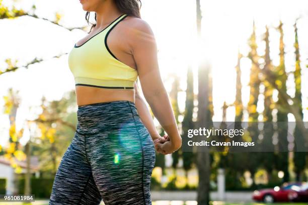 midsection of woman stretching arms behind back while exercising in park - sportbeha stockfoto's en -beelden