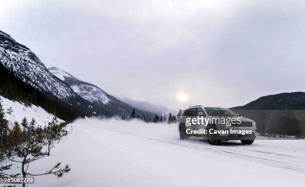 off-road vehicle moving on snowy field against cloudy sky - winter car stock-fotos und bilder