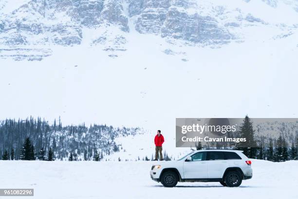 hiker standing on snow covered field by off-road vehicle during winter - snow covered road stockfoto's en -beelden