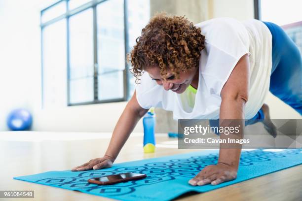 happy woman looking at smart phone while exercising in yoga studio - short hair for fat women stock pictures, royalty-free photos & images