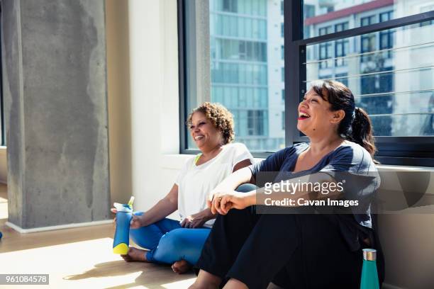 happy female friends sitting against window in yoga studio - fat people stock pictures, royalty-free photos & images